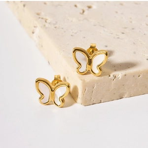 Detailed macro shot of 18K gold butterfly earrings with white shell on beige stone