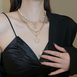 Detail of layered gold necklace with star charms and white pearls on a model wearing black