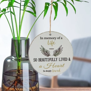 Memorial Christmas ornament with angel wings and gold script hanging on a green tree