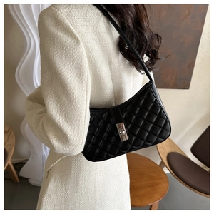 Détail d'un sac bandoulière matelassé noir avec fermoir métallique porté à l'épaule