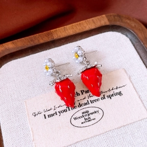 Detailed shot of red strawberry earrings with white flower and silver leaf on wood