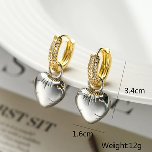 Detailed view of gold hoop earrings with silver heart charms and zircon stones on a white tray