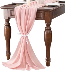 Detail of pink chiffon table runner tied with a white ribbon bow on a dark wood table