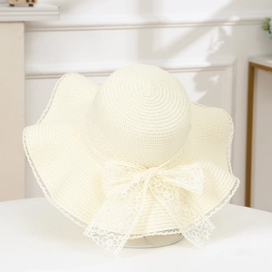 Detailed view of the wide-brimmed straw hat featuring a delicate lace bow and wavy edges