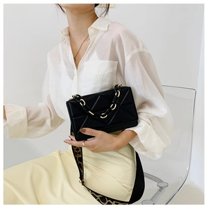 Close-up of black quilted leather crossbody bag with gold chain and lettered strap
