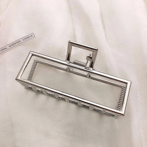 Close-up of a silver rectangular hollow metal hair claw clip on white satin background