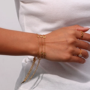 Detail of layered gold-plated bracelets and rings worn on hand against a white knit background