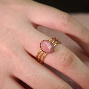 Detail of gold triple-band ring set with a faceted oval pink gemstone on finger
