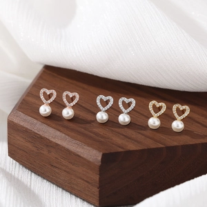 Elegant heart-shaped pearl earrings with micro-diamonds displayed on a walnut wooden stand