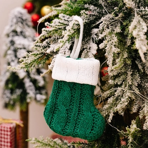 Close-up of green knitted Christmas mini stocking hanging on a snow-dusted tree branch