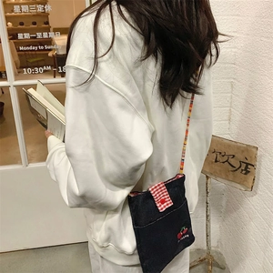 Mini denim crossbody bag with cherry embroidery and colorful beaded strap worn on person