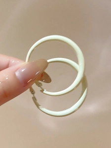 Close-up of matte cream-colored hoop earrings held by hand against a soft background