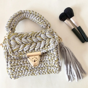 Detail of grey handmade crochet crossbody bag with gold lock and decorative tassels