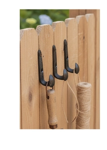 Three vintage black cast iron J-hooks mounted on a wooden fence with gardening tools
