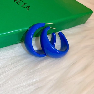 Detail of royal blue glossy C-shape hoop earrings on white faux fur background