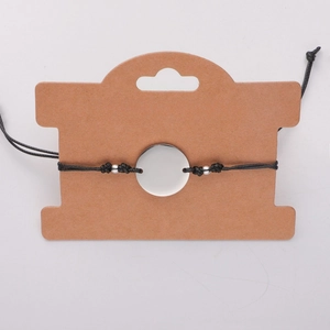 Detail of adjustable black wax rope bracelet with polished silver round charm on card