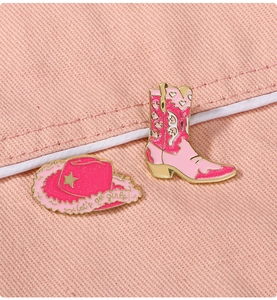 Close-up of pink enamel cowboy boot and hat pins with Let's Go Girls text on denim