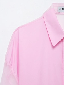 Dettaglio della camicia rosa con colletto a punta e maniche in organza trasparente