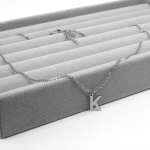 Close-up of silver stainless steel necklace with capital letter K pendant on a tray