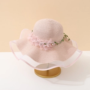 Détail d'un chapeau de paille rose avec fleurs en soie décoratives et bord en dentelle