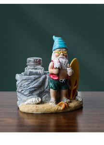 Detail of beach gnome resin holder with surfboard and glass spice shaker on wood desk