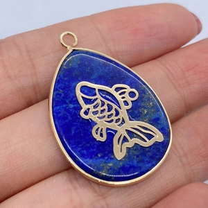 Macro detail of teardrop lapis lazuli pendant with golden koi fish inlay held in hand