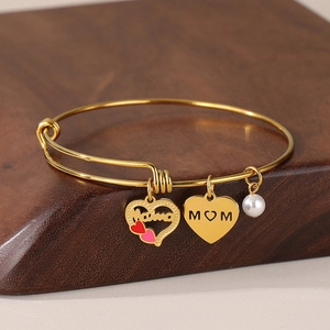 Detailed shot of golden MOM heart charms and white pearl on an adjustable bracelet
