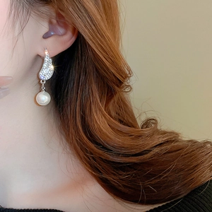 Close-up of wing-shaped silver earrings with sparkling zircon and white pearl drop