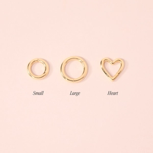 Detailed view of gold round and heart-shaped jewelry clasps on light pink backdrop