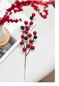 Close-up of artificial red berries and dark purple foam stems on a white table setting