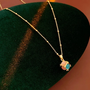 Detailed close-up of a gold-plated necklace with opal cube pendant on green velvet
