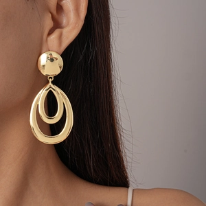 Detail of model wearing double oval gold metal drop earrings on a grey background