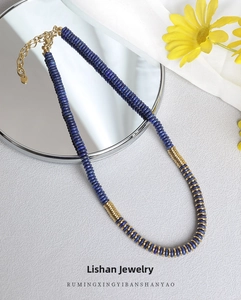 Lapis lazuli beaded necklace with golden metal spacers on elegant light gray background