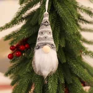 Close-up of a knitted Christmas gnome ornament with white beard hanging on a pine tree