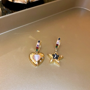 Macro shot of asymmetric gold earrings with heart and star charms featuring colored gems