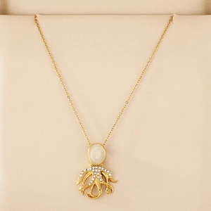 Close-up of golden octopus pendant with white enamel and sparkling crystals on beige velvet
