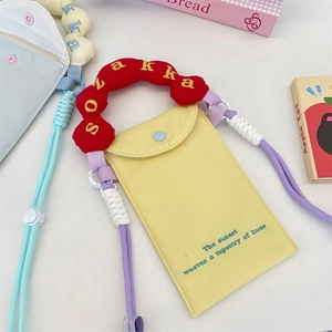 Détail du sac de téléphone en toile jaune avec poignée peluche rouge et bandoulière