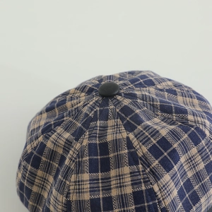 Detailed macro view of the navy and beige plaid fabric and matte button on the baker boy hat