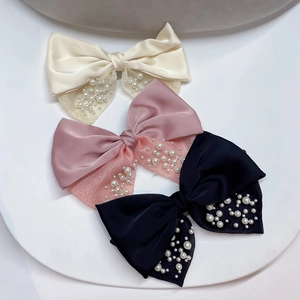 Dettaglio di tre fermagli a fiocco in raso con perle nei colori bianco, rosa e nero