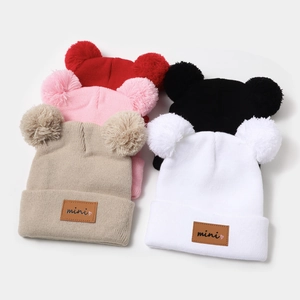 Detail view of colorful knit beanies for kids with soft fur pom-poms and leather mini labels