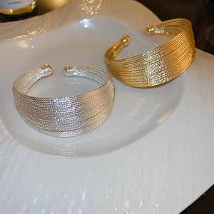 Dettaglio di bracciali rigidi a strati oro e argento con trama metallica su un piatto bianco