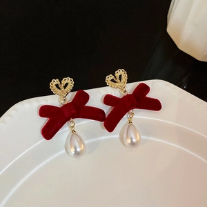 Detail of red velvet bow earrings with gold heart studs and pearl drops on a white plate