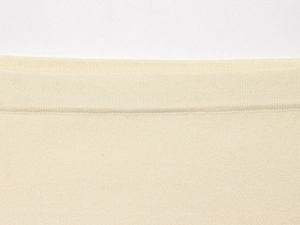 Detailed macro view of the cream knitted fabric texture and ribbed hem craftsmanship