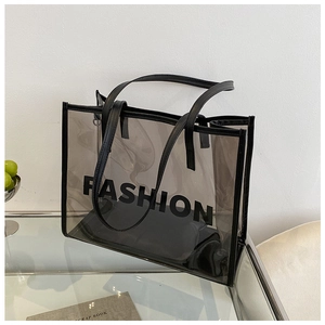 Close-up of a clear PVC tote bag with black trim and FASHION lettering on glass table