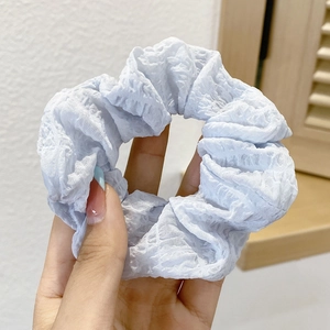 Detail shot of a light blue pleated scrunchie hair tie held by hand against a soft background