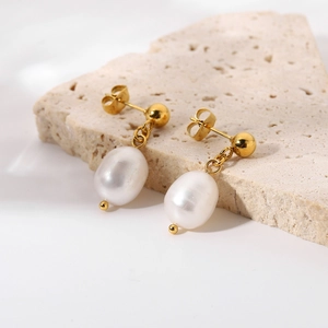 Detail shot of gold-plated drop earrings with large white oval pearls on textured stone