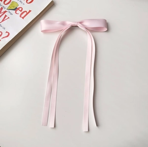 Detailed view of pink satin bow hair clip with long ribbon tails on a neutral background