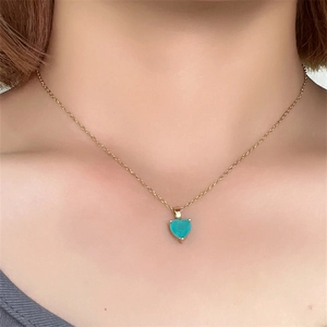 Close-up of a heart-shaped turquoise stone pendant with a gold chain worn on the neck