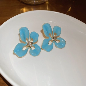 Détail macro de boucles d'oreilles fleurs en émail bleu avec bord doré et zircon