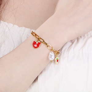 Detail of gold strawberry pearl bracelet on wrist with dainty charms and chunky chain